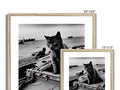 A cat is sitting on top of wooden framed photo of a boat with two people in