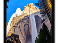 A cliff face with snow, mountains, trees and a crashing waterfall on it by a