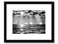 A black and white framed print of the ocean with a sailboat passing by a house