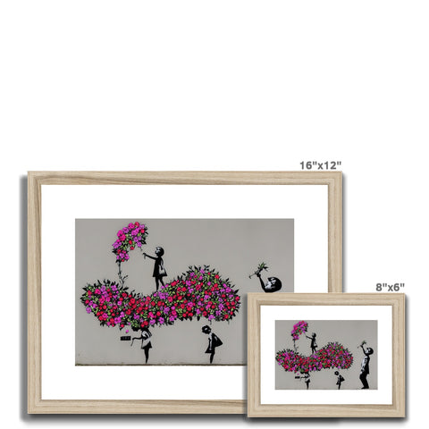 A wooden framed art print of an individual tree and picture of flowers on the wall.