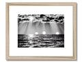 A picture of a white sunset on the water in a frame on a wooden shelf.