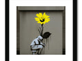 An art print on a wall standing next to a large yellow flower.