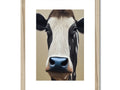 a cow standing in a field looking at a wood framed image of cows