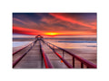 A colorful sunset view of a boogie boarding pier with an art print on the shore