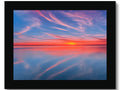 A light blue framed picture with a sunset in the sky overlooking a water, surrounded by