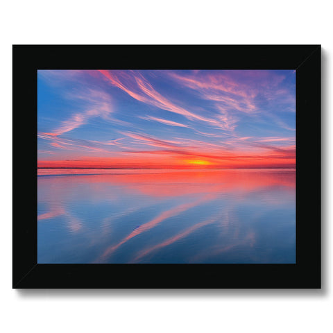 A light blue framed picture with a sunset in the sky overlooking a water, surrounded by