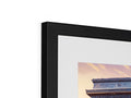 A photo is on top of a piece of art in a brown framed photo frame.