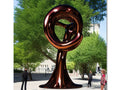An oval colored circle standing in front of a large metal sculpture.