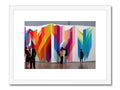 An art print hanging over colorful artwork in a white wall.
