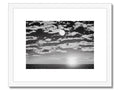 A black and white framed picture with a black and yellow sun and a moon setting in
