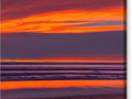 The ocean that is lit with a bright orange background and some sunset is reflected in a