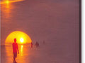 An orange sunset is shown above a giant blue ball on a beach
