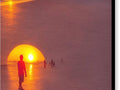 An orange sunset is shown above a giant blue ball on a beach