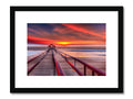 A picture of a beautiful beach at sunset hanging from a black frame and framed by wood