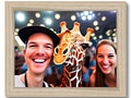 A giraffe holding a wooden photo frame that has two people standing beside him.