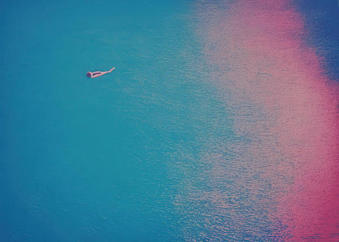 A person in the ocean has a pink surfboard sitting in the water.
