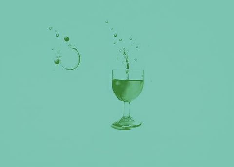 A green and white bottle of wine sitting on top of an empty glass.