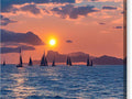 a large group of very large sail boats sitting on that water at sunset