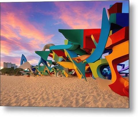 A piece of art next to the sand covered beach with some colorful tents