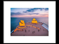 A table with two reclining orange chairs at a beach that has four slides on it