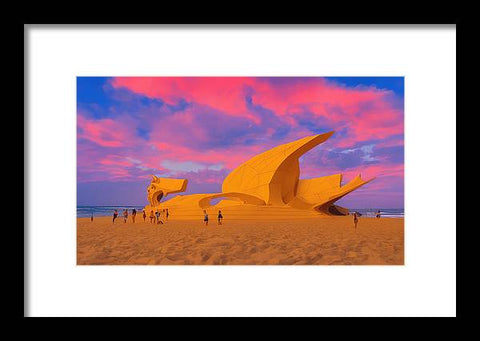 An art print sits on a cliff overlooking the water with a sunset